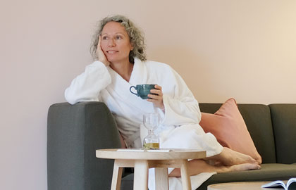 Person sitzt auf der Couch mit einer Tasse in die Hand, Bewusster Verzicht: Warum ist fasten eigentlich gesund, Kurhaus, Retreat und Healthresort Marienkron