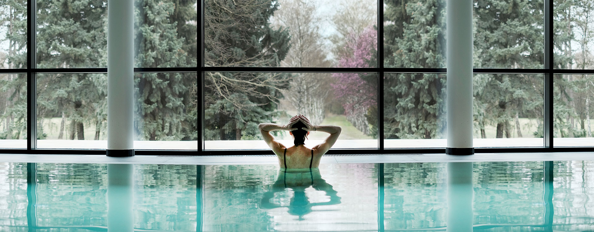 Ansicht Pool mit einer Person die auf die große Fensterwand mit Ausblick in die Natur sieht, Home, Kurhaus, Retreat und Healthresort Marienkron